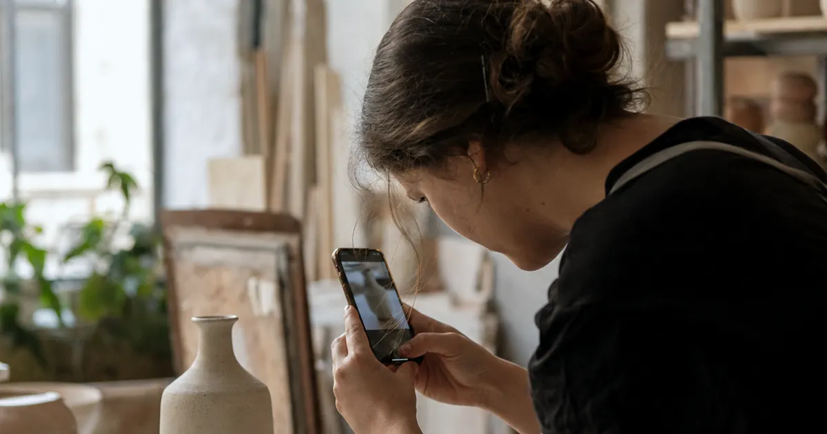 Seramik atölyesinde el yapımı vazoyu telefonuyla fotoğraflayan bir zanaatkâr