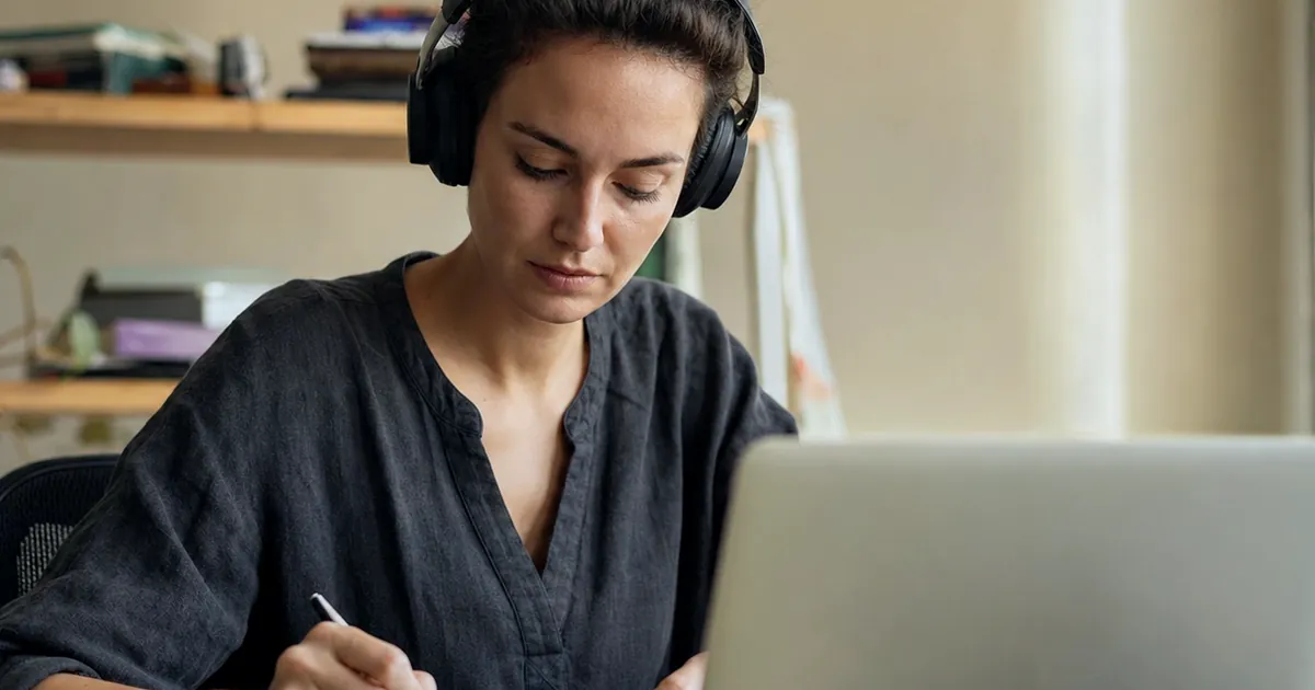 Kulaklıkla laptop başında çalışıp not alan bir kadın