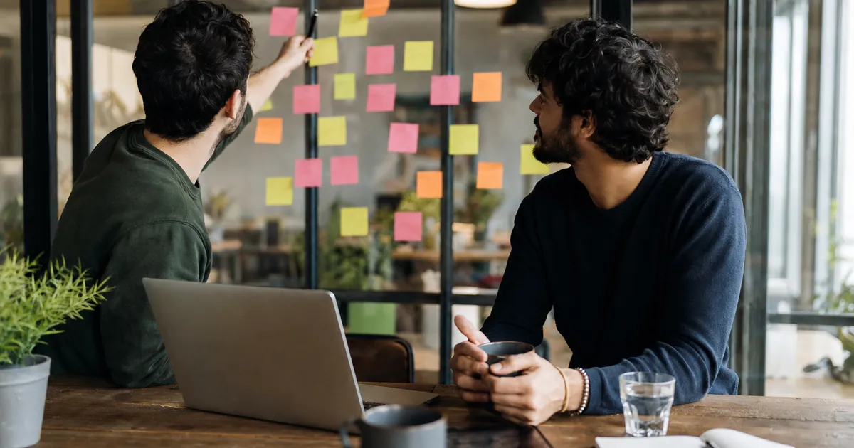 Cam duvara yapıştırılmış renkli notlarla yeni e-ticaret sitesini planlayan iki girişimci