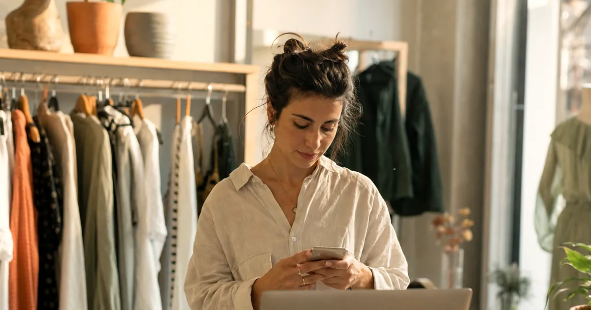 Küçük bir mağazada telefonundan müşteri mesajlarına bakan bir işletme sahibi