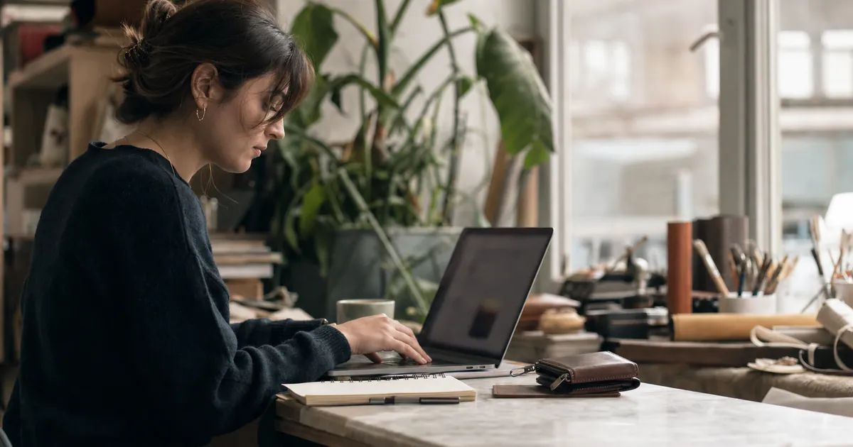 Masada ürünü yanına koyup laptopta açıklama yazan bir kadın